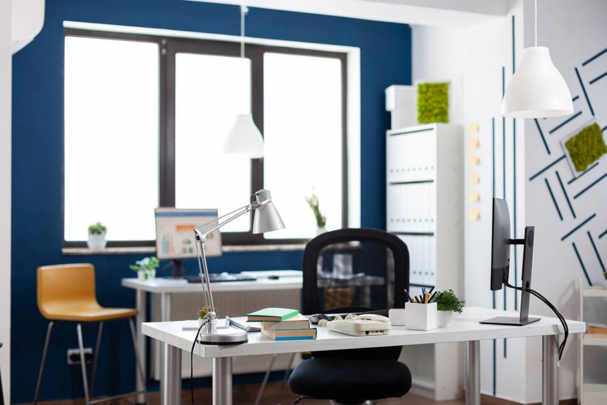 Modern office space with a white desk, ergonomic chair, and vibrant blue walls, decorated with minimalist shelves and white lamps.