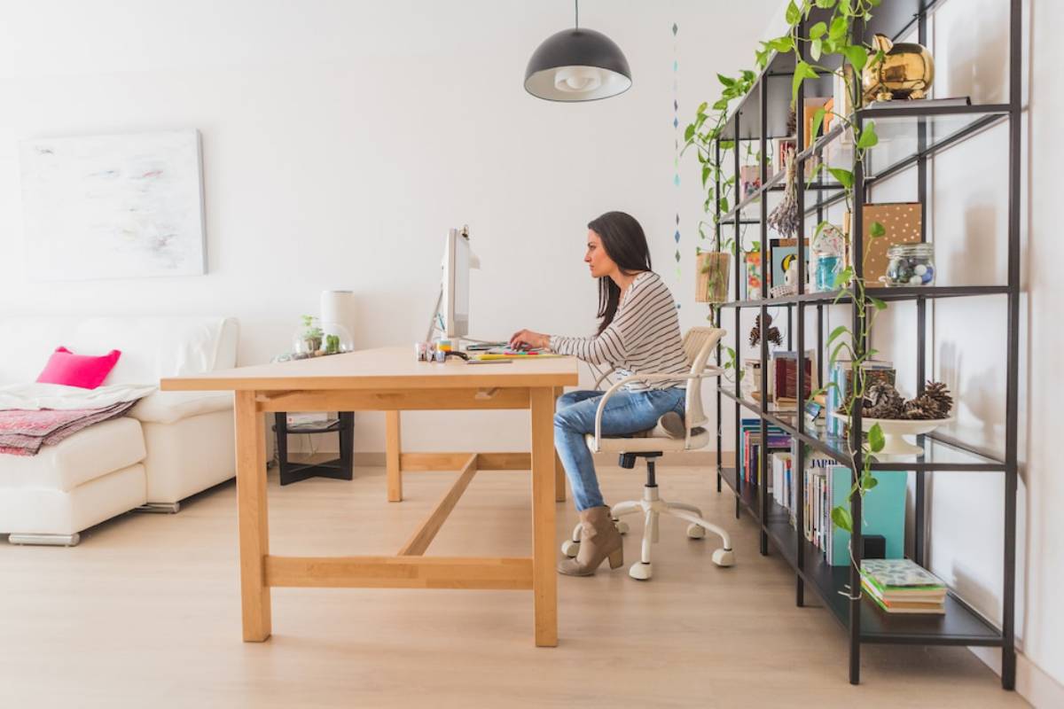 Woman working on computer at wooden desk in a bright, plant-decorated home office.