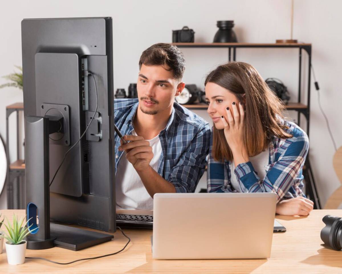Two young adults, a man and a woman, looking at a computer screen together in an office setting.