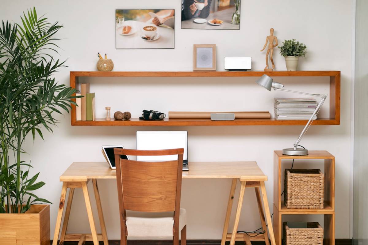 Home office with a desk, chair, and shelves filled with books and personal items, flanked by indoor plants.