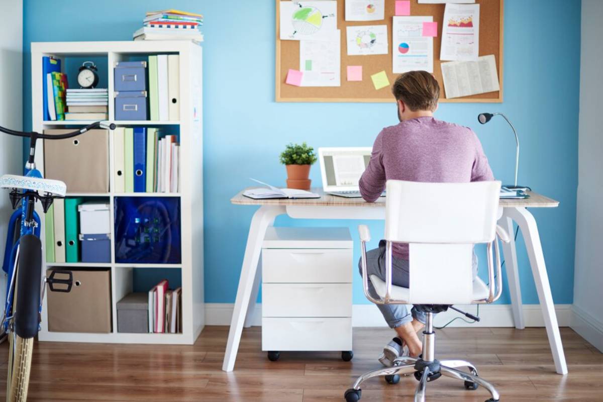 Man sitting at a desk in a neat, organized home office with a blue wall and vibrant decor.
