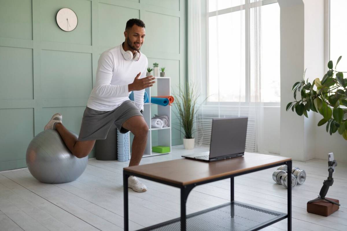 Man exercising at home, performing a lunge near a laptop and exercise equipment.