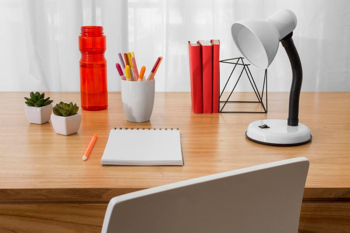 A desk featuring a lamp, an open notebook, and a steaming cup of coffee, creating a cozy workspace atmosphere.