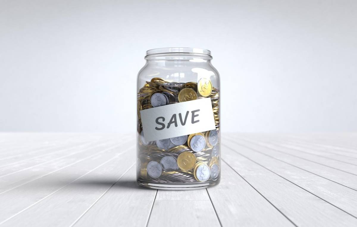 Glass jar filled with coins labelled save on a wooden surface.