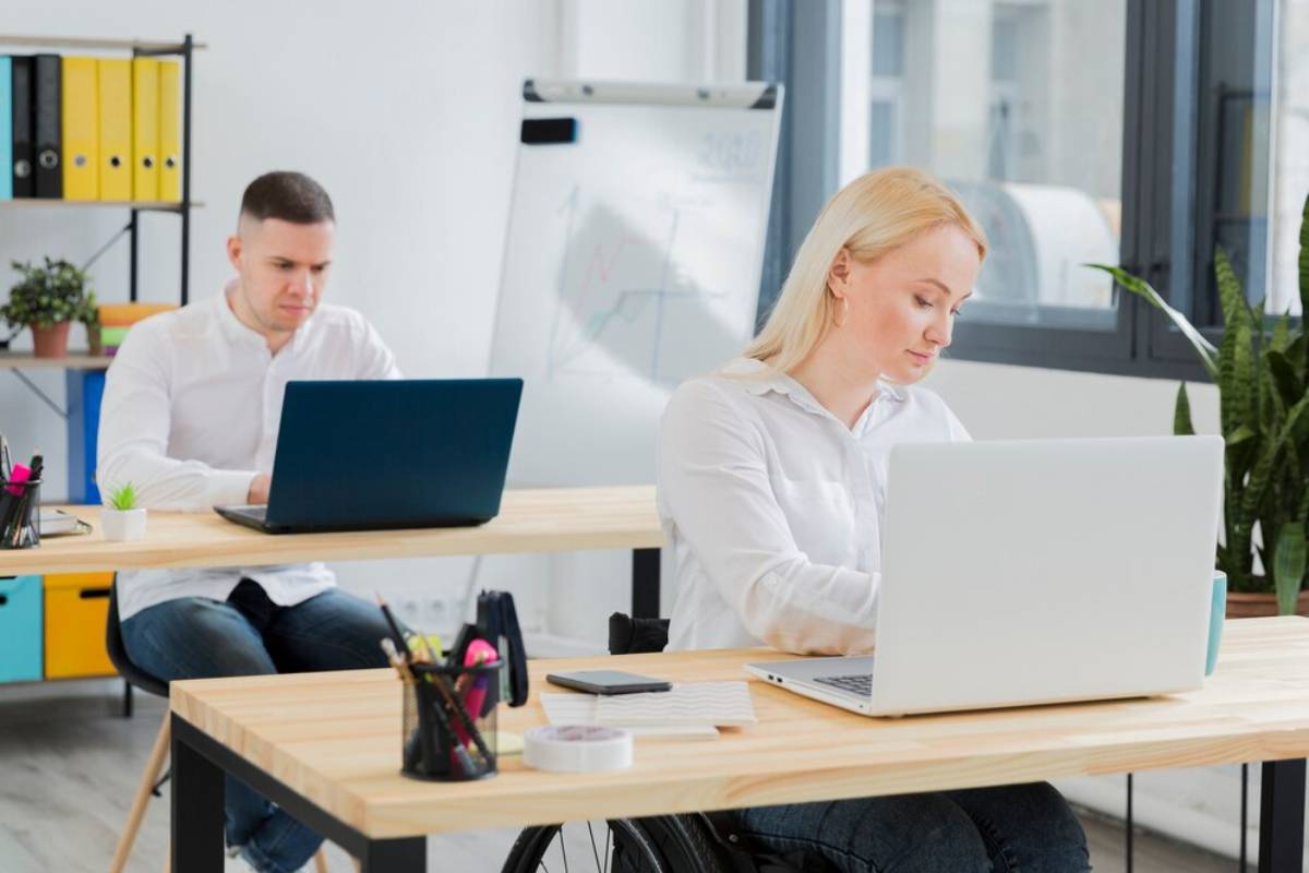 Two professionals working on laptops in a bright, modern office space.