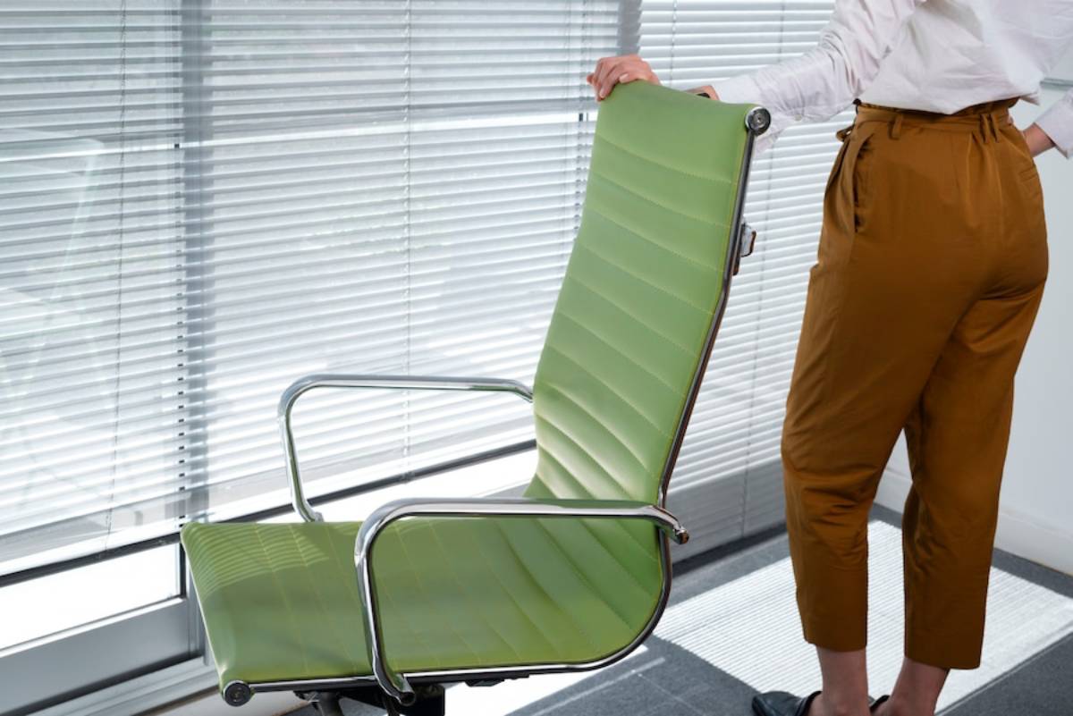 A woman stands beside a green office chair in a modern workspace.