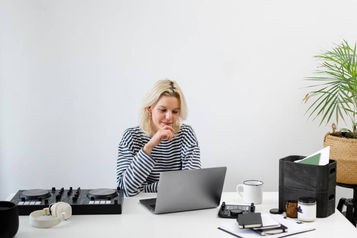 A woman focused on her laptop at a modern, tidy desk, surrounded by DJ equipment and office supplies.