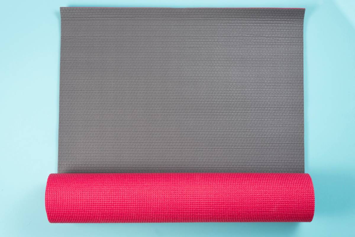 A yoga mat with a red roll placed on top, ready for a workout or relaxation session.