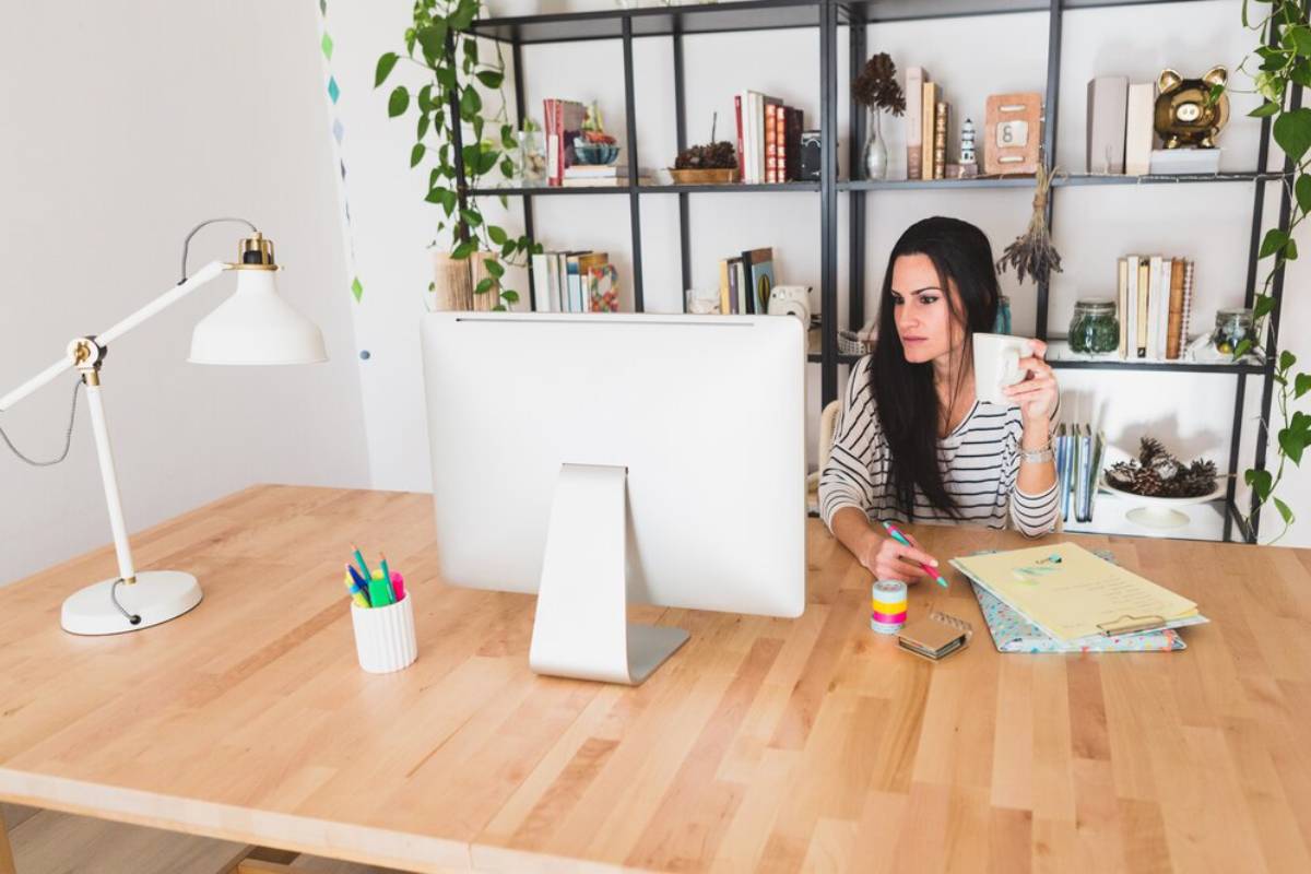 Woman sitting at a modern home office desk, working on a computer with a cup of coffee.