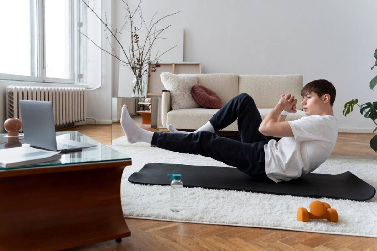 Man doing abdominal exercises on a mat in a bright living room with laptop and weights nearby.