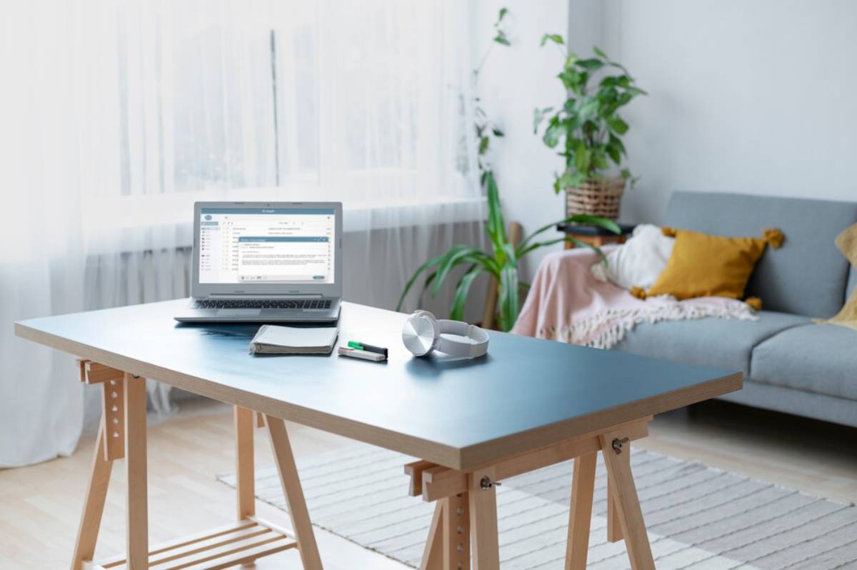 A modern home office setup with a laptop, headphones, and notepad on a minimalist desk; cozy living area with plants in the background.