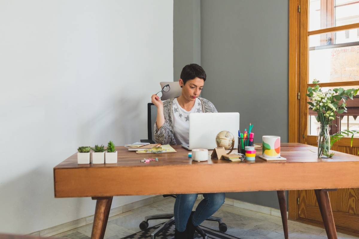 A woman seated at a desk, focused on her laptop, with a notepad and pen beside her.