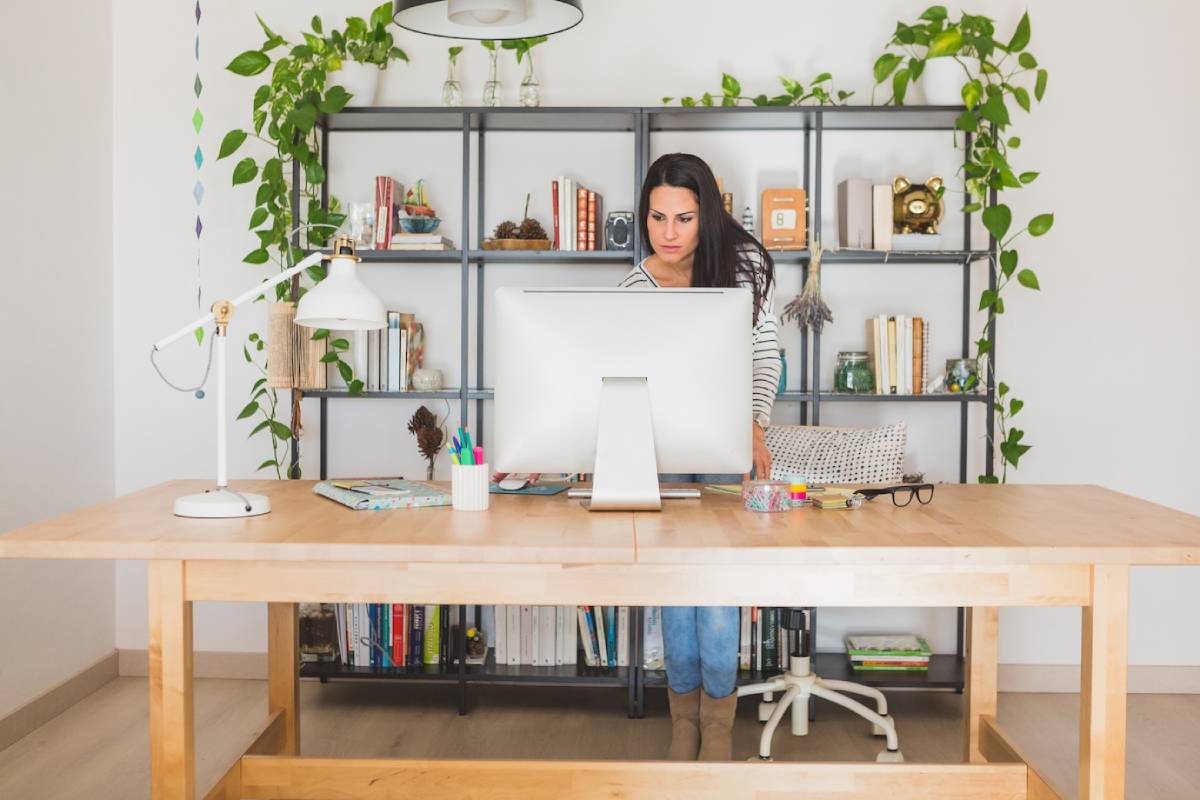 A woman sits at a desk, focused on her computer, with papers and a coffee cup nearby. 