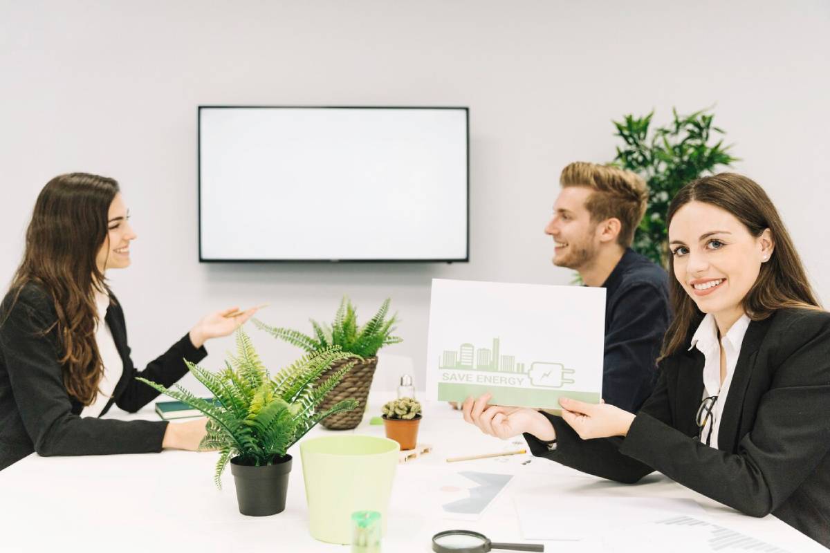 Three business professionals seated at a table, discussing strategies in front of a green presentation board. 