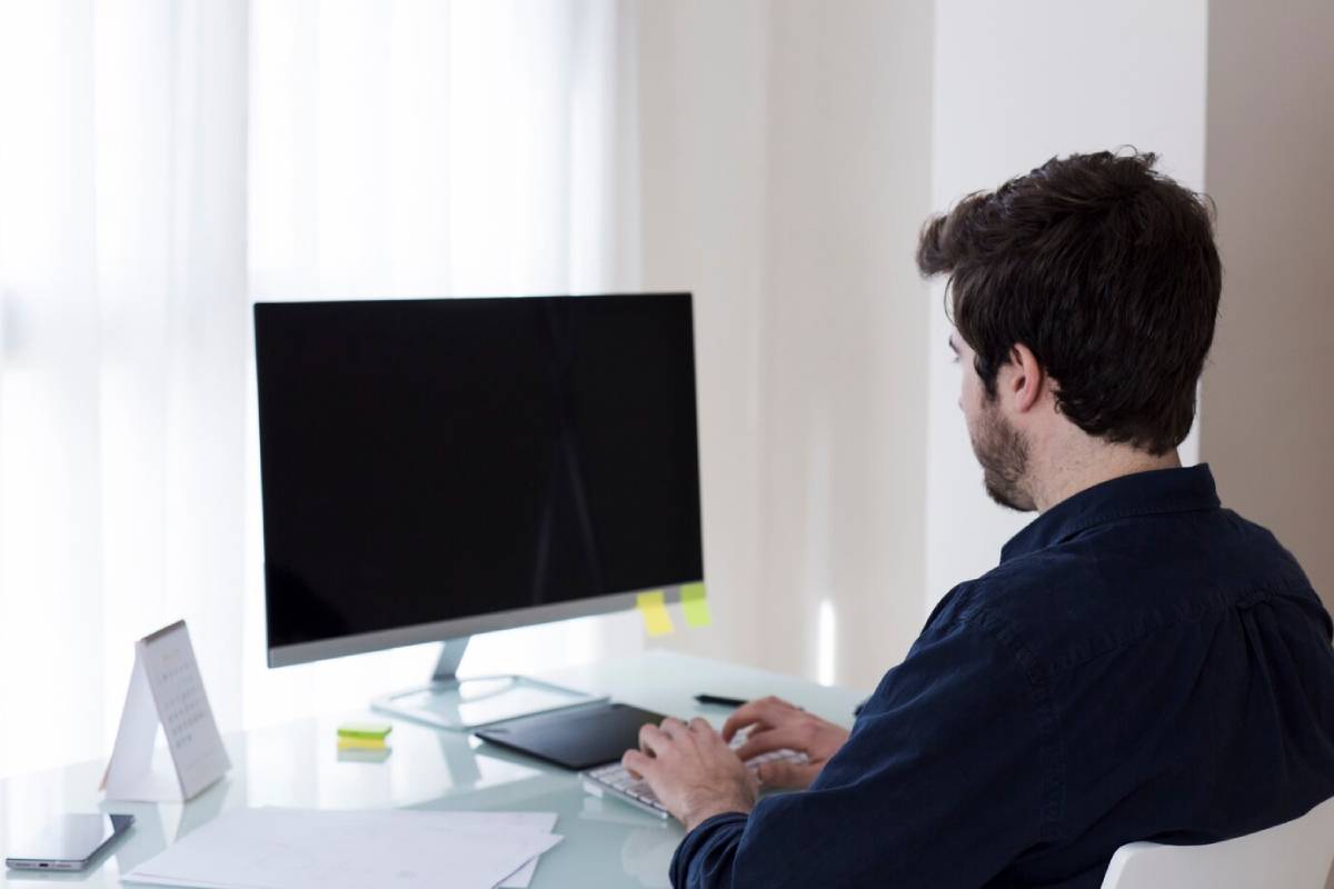 A man seated at a desk, working on a computer and a laptop, focused on his tasks.
 