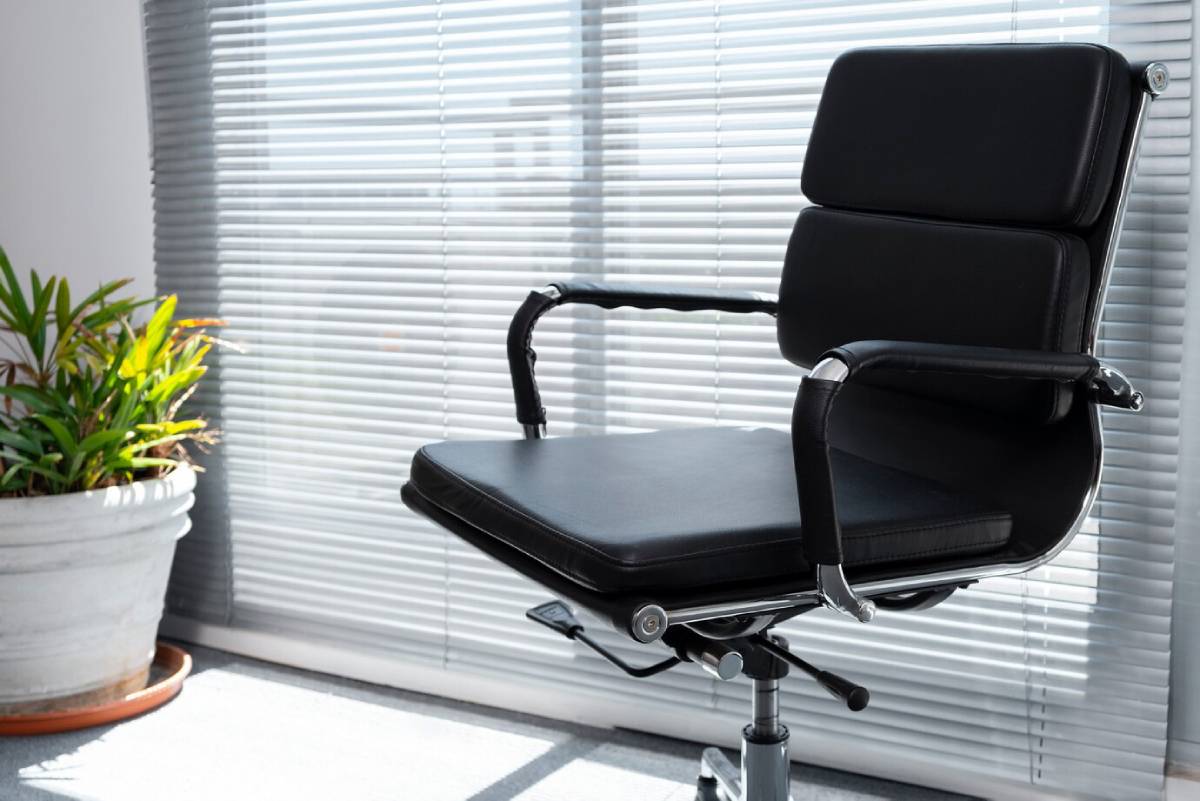 Black office chair positioned in front of a window with closed blinds, creating a professional workspace atmosphere.