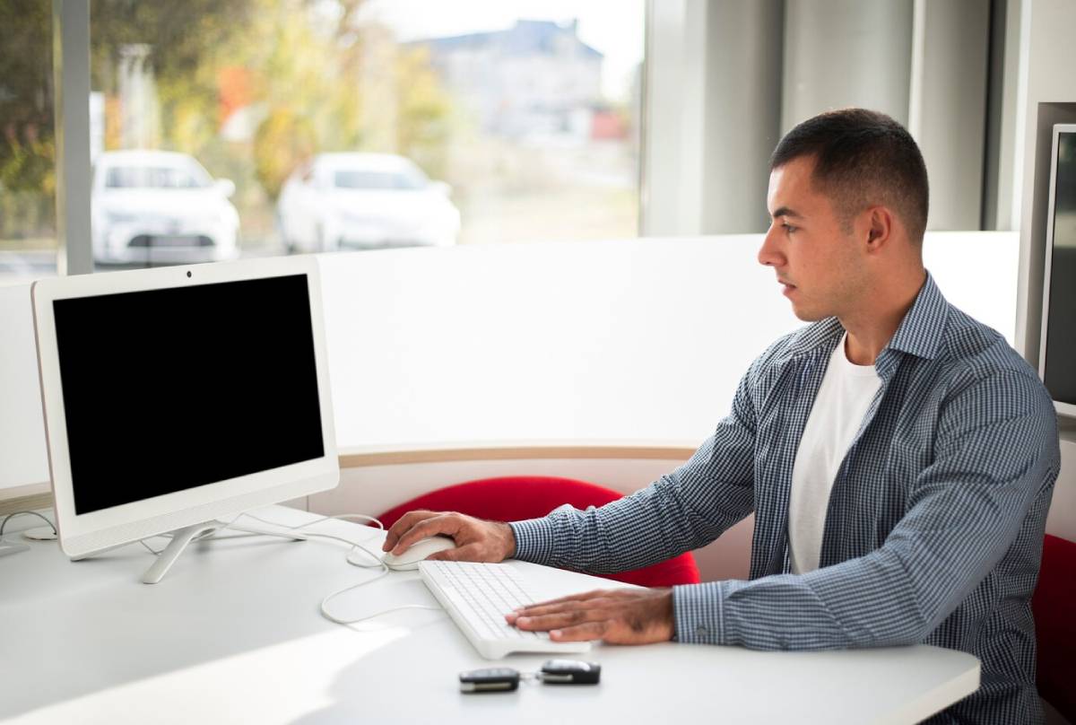  A man seated at a desk, working on a computer with a keyboard in front of him.